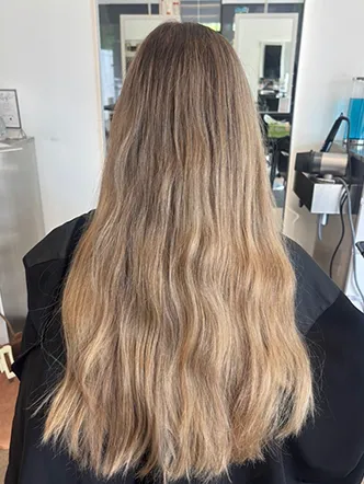 Person with long, wavy, light brown hair, seated in a salon chair facing away from the camera at the best hair salon in Franklin TN, with mirrors and salon equipment visible in the background. | Salon Blonde in Columbia, TN, Spring Hill, TN, Franklin, TN