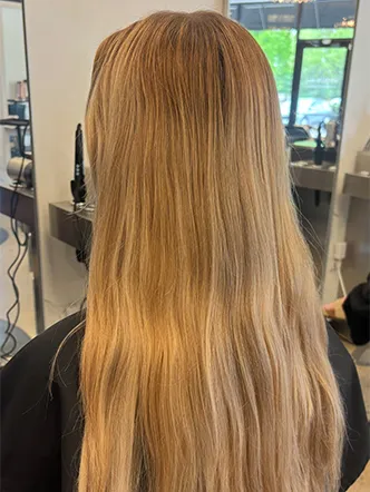 Person with long, straight, light brown hair seen from behind, sitting in a salon chair with salon mirrors and equipment visible in the background at the best hair salon in Franklin TN. | Salon Blonde in Columbia, TN, Spring Hill, TN, Franklin, TN