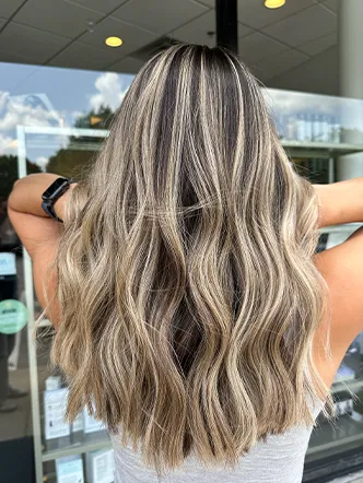 Person with long, wavy blond hair featuring dark roots and lighter highlights stands outside a building, seen from behind—a stunning look that’s reminiscent of the styles offered at the best hair salon in Franklin TN. | Salon Blonde in Columbia, TN, Spring Hill, TN, Franklin, TN