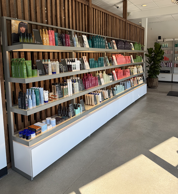 Shelves in a salon display various hair care products, including shampoos, conditioners, and styling items, arranged by color and type along a well-lit, modern wall. | Salon Blonde in Columbia, TN, Spring Hill, TN, Franklin, TN