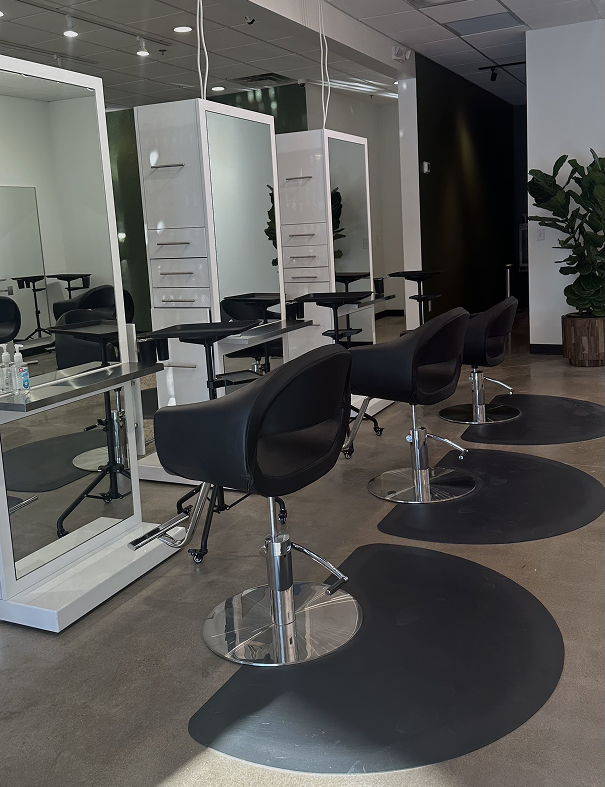 Three black salon chairs face individual mirrors and stations in a modern, well-lit hair salon with a plant in the corner and clean concrete floors. | Salon Blonde in Columbia, TN, Spring Hill, TN, Franklin, TN